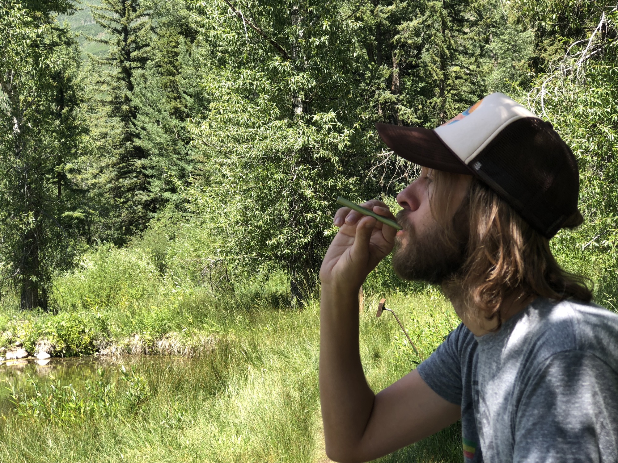 Man inhaling MONQ forest diffuser beside a still pine-forest pond — forest bathing engages the olfactory pathway through airborne terpenes