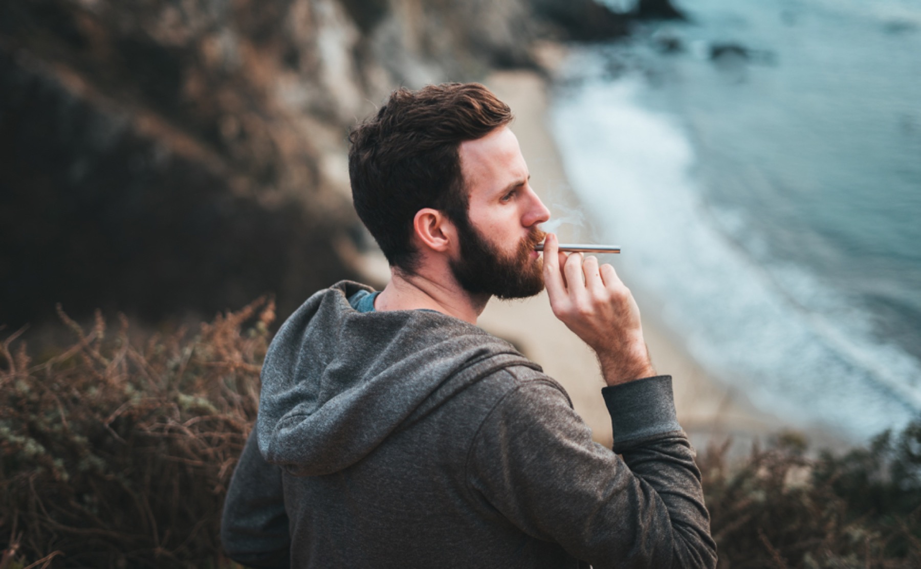 Man using MONQ diffuser at ocean cliffs — portable botanical aromatherapy designed for the moments modern life actually looks like