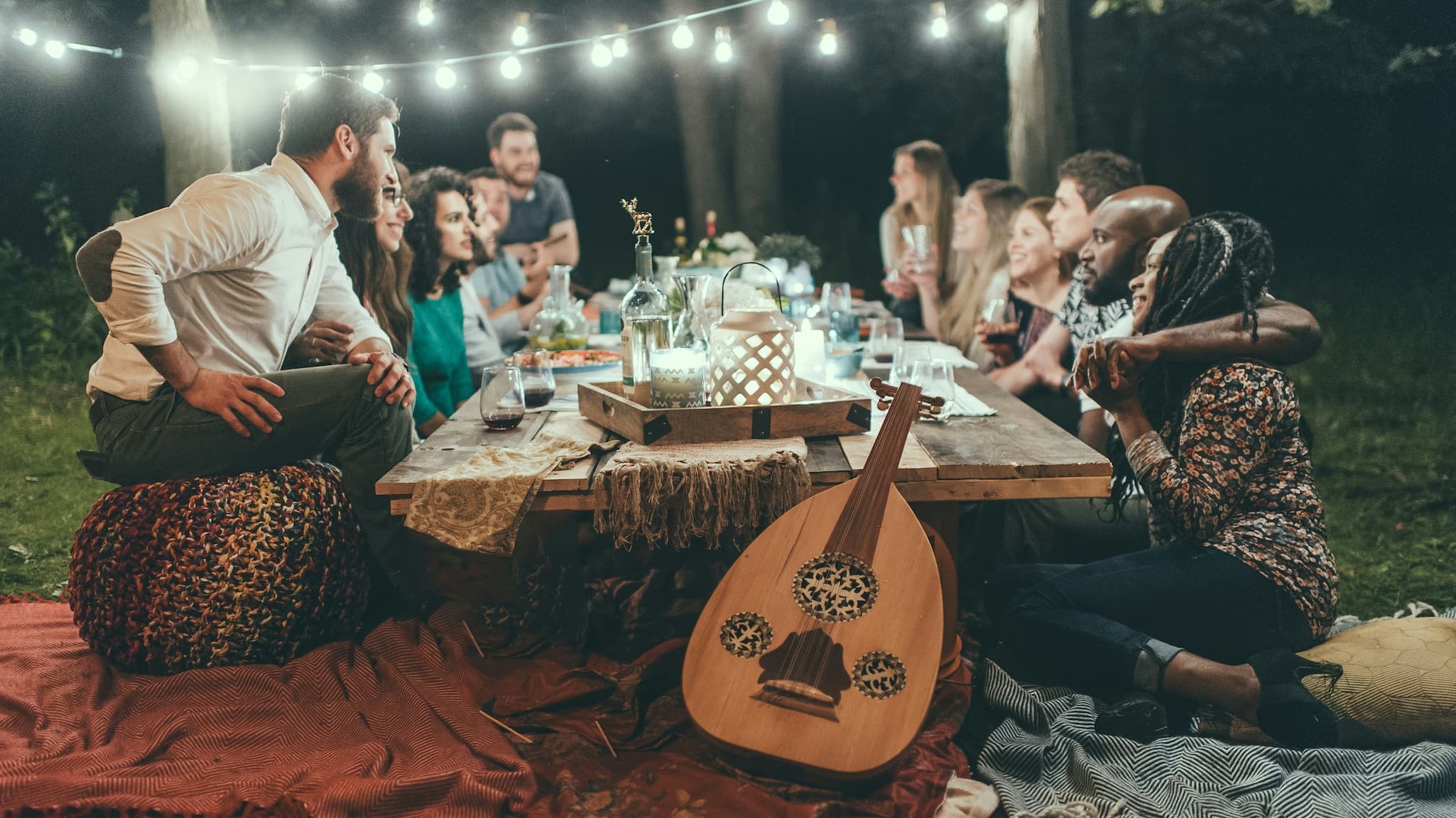 a group of people sitting at a table having food and drinks in the evening in a backyard