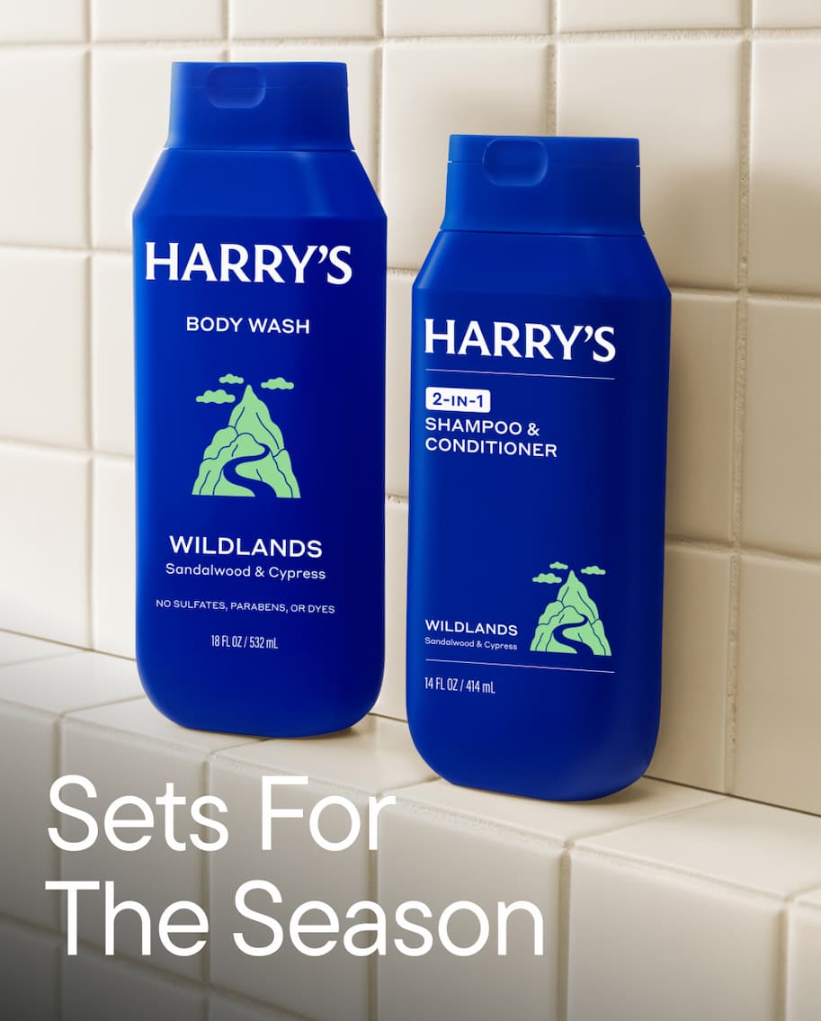 Two Harry's body wash bottles. Mid-Glades scent and a blue variant — surrounded by foliage, with the headline: Sets For The Season