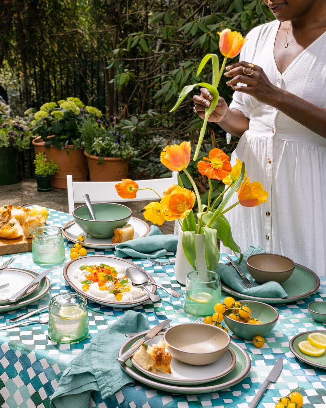 A woman picks up a tulip from a color-drenched tabletop on a patio