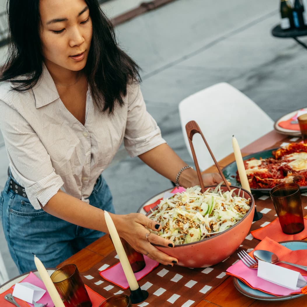 A women places a Mixing Bowl in Guava with a fennel salad in it onto a brightly style table. A women places a Mixing Bowl in Guava with a fennel salad in it onto a brightly style table.