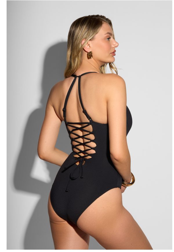 A woman wearing a black swimsuit with a lace-up back, standing sideways.