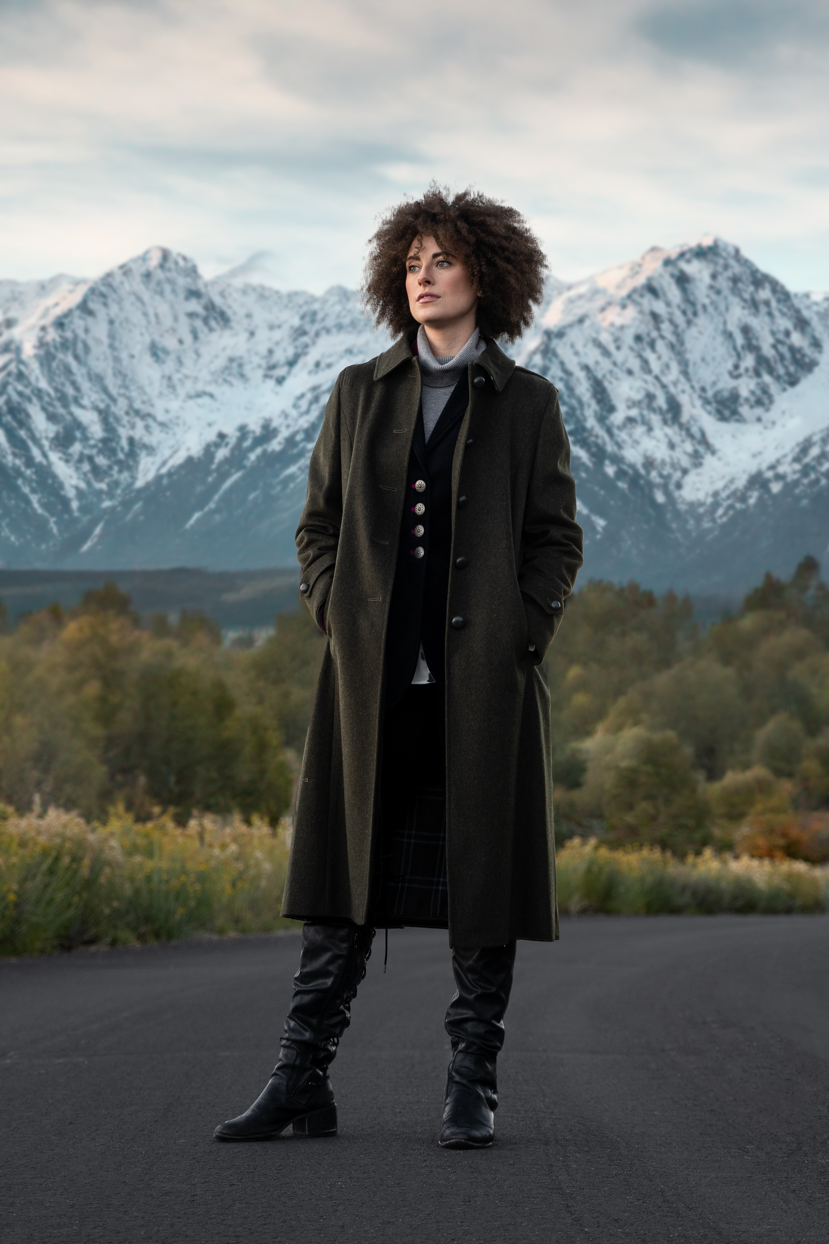 beautiful young women wearing a Robert W. Stolz Loden Coat in green, standing in a road with dramatic mountains in the background