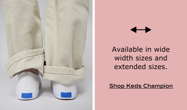 The back of the Keds Champion Canvas Lace-Ups in white shown on foot paired with light khaki-colored pants cuffed in order to show the iconic Keds blue heel logo. White text on a blush background says Available in wide width sizes and extended sizes. Shop Keds Champion.