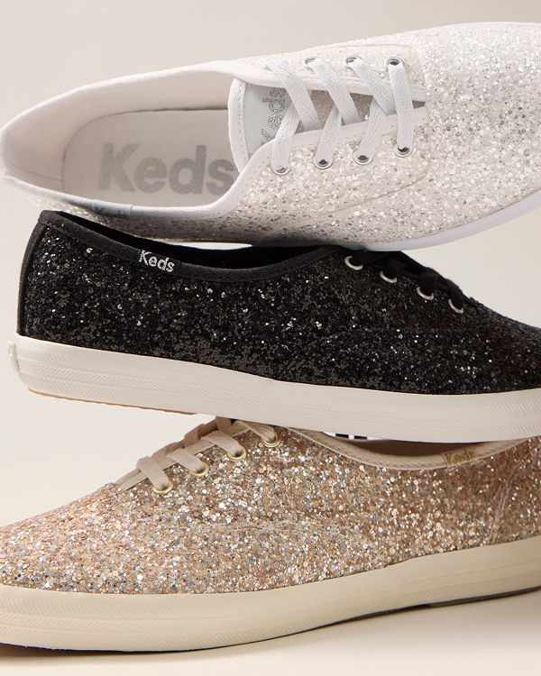Three different colors of Keds Champion Glitter Lace-Ups stacked on top of one another: gold, black, and white.
