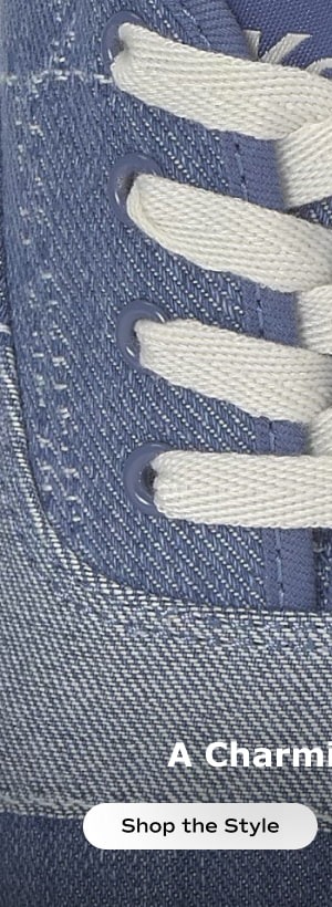A zoomed-in view of the top of the Keds Champion Denim Patchwork Charm Lace-Up in navy showcasing the white cotton laces and two lace charms, a flower and a heart. Shop the style.