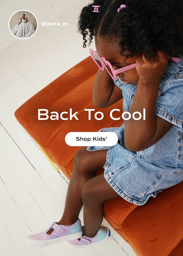 Kids' style influencer @jezra_m sits on a burnt orange velvet ottoman. She is wearing pink heart sunglasses, a light-wash denim dress, and the little kids' Daphne sneaker in multicolor ombre sequins. Text over the image reads, "Back to Cool. Shop Kids'."