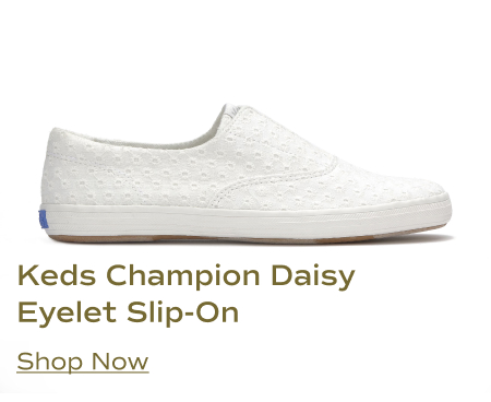 A side view of the Keds Champion Daisy Eyelet Slip-On sneaker in snow white. It features an all-over daisy eyelet pattern on the upper, a slip-on design, and a white rubber sole. Shop Now.