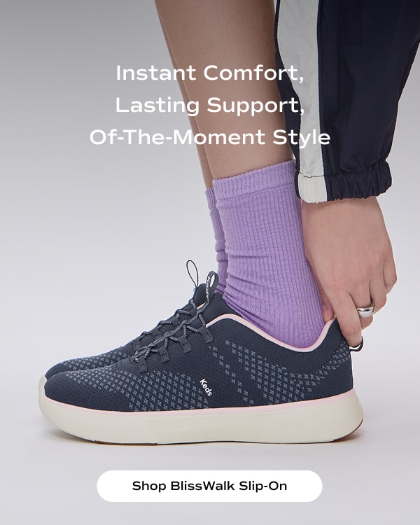 Instant Comfort, Lasting Support, Of-The-Moment Style. A closeup of a woman wearing purple socks paired with the BlissWalk Slip-On in navy. Shop BlissWalk Slip-On.
