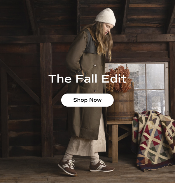 A woman in a cozy log cabin dressed in a layered fall outfit: a cream beanie, long trench coat, beige knitted maxi skirt, scrunched beige socks, and the Rena Nylon/Suede Lace-Up in chocolate. The email says The Fall Edit. Shop Now.
