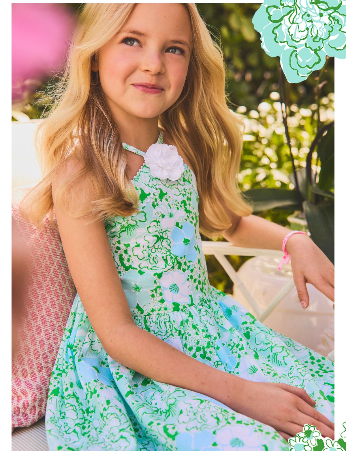 Young girl wearing a green and blue floral print halter dress with a white flower corsage, seated outdoors