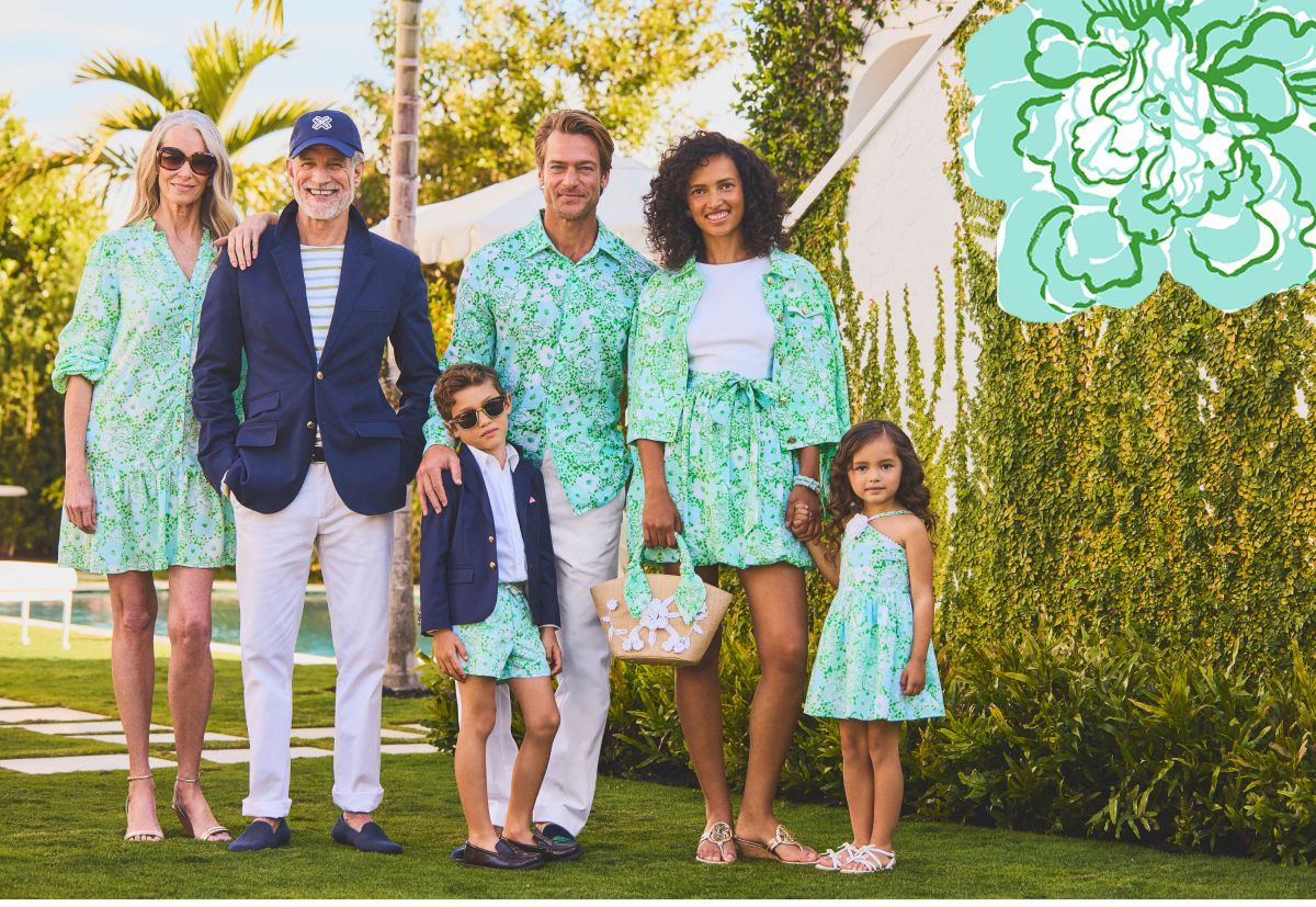A multigenerational family wearing coordinating green and blue floral Lilly Pulitzer outfits posed outdoors near a pool and lush greenery