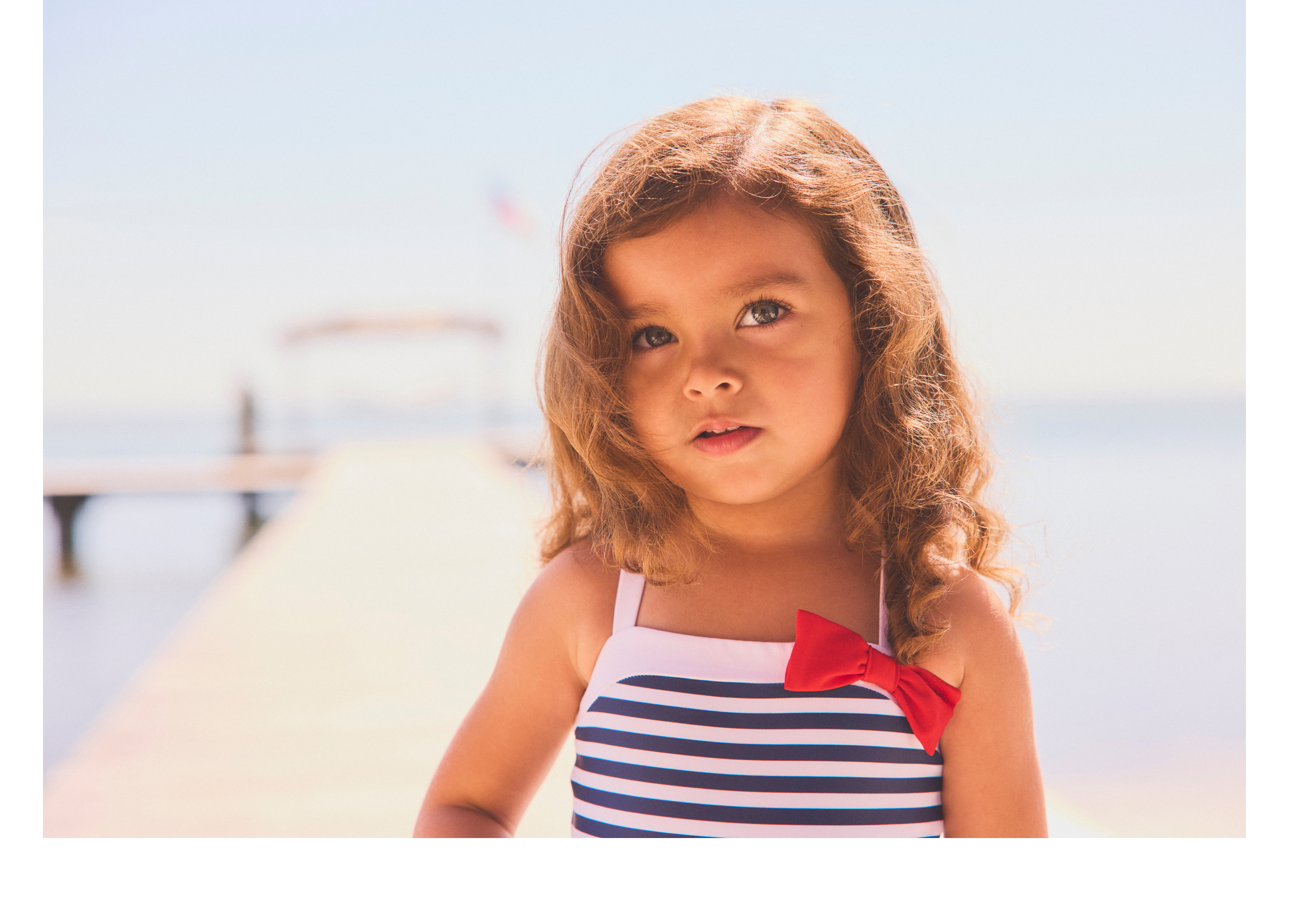 Young girl in navy striped swimsuit with red bow on a pier