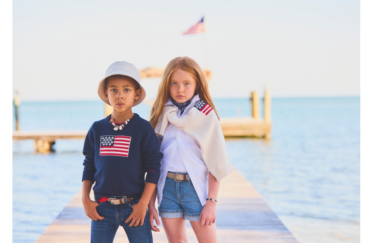 Two children wearing American flag apparel standing by water with wooden dock in background