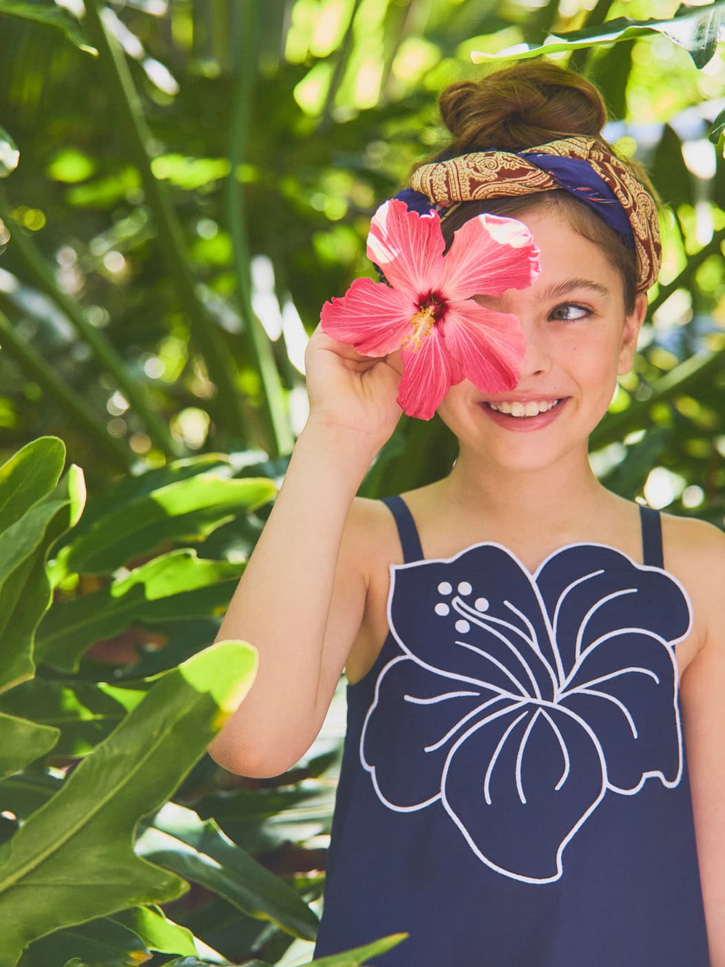 Young girl holding pink hibiscus flower wearing navy swimsuit with floral design