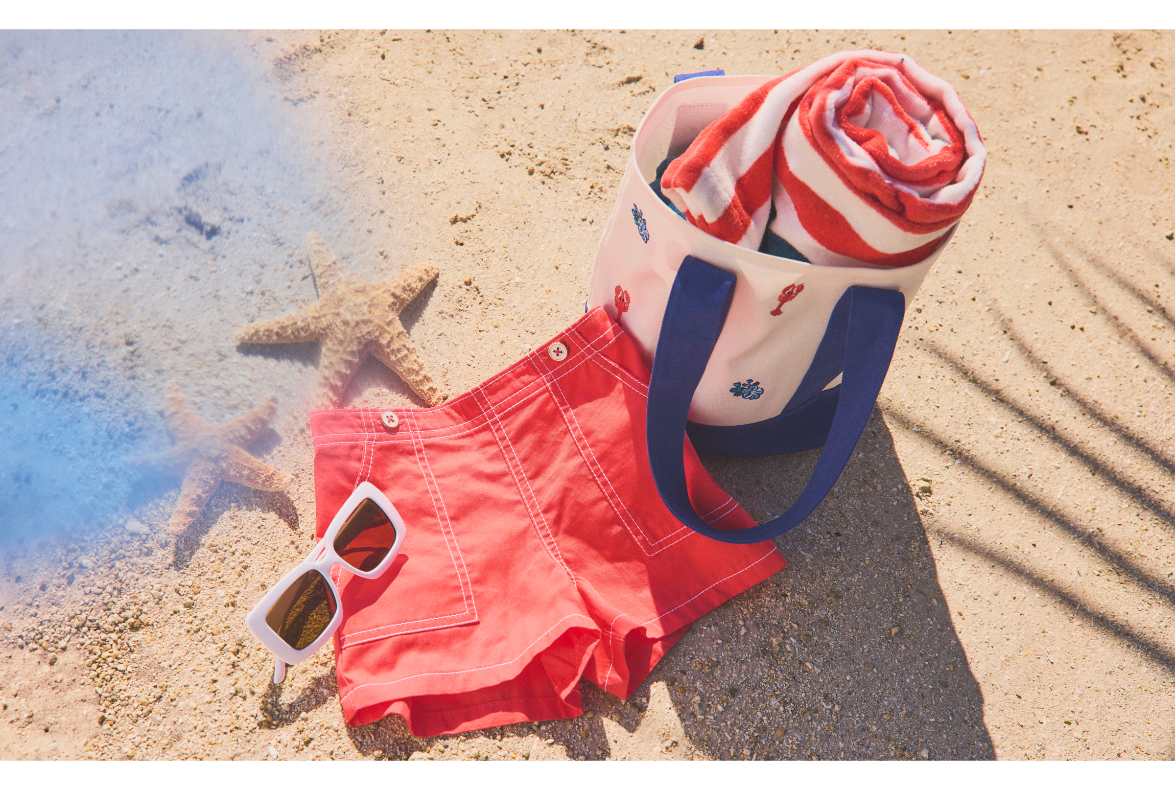 Beach scene with red swim shorts, white sunglasses, striped towel in beach bag, and starfish on sand