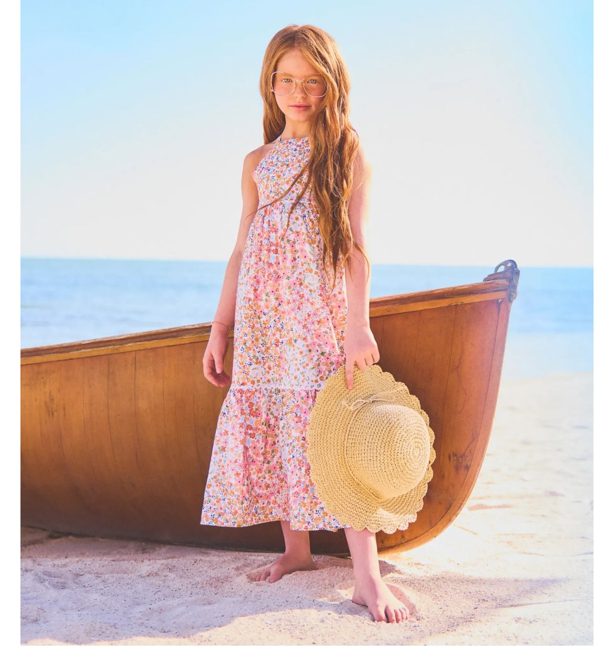Girl on the shore holding a hat in a floral dress