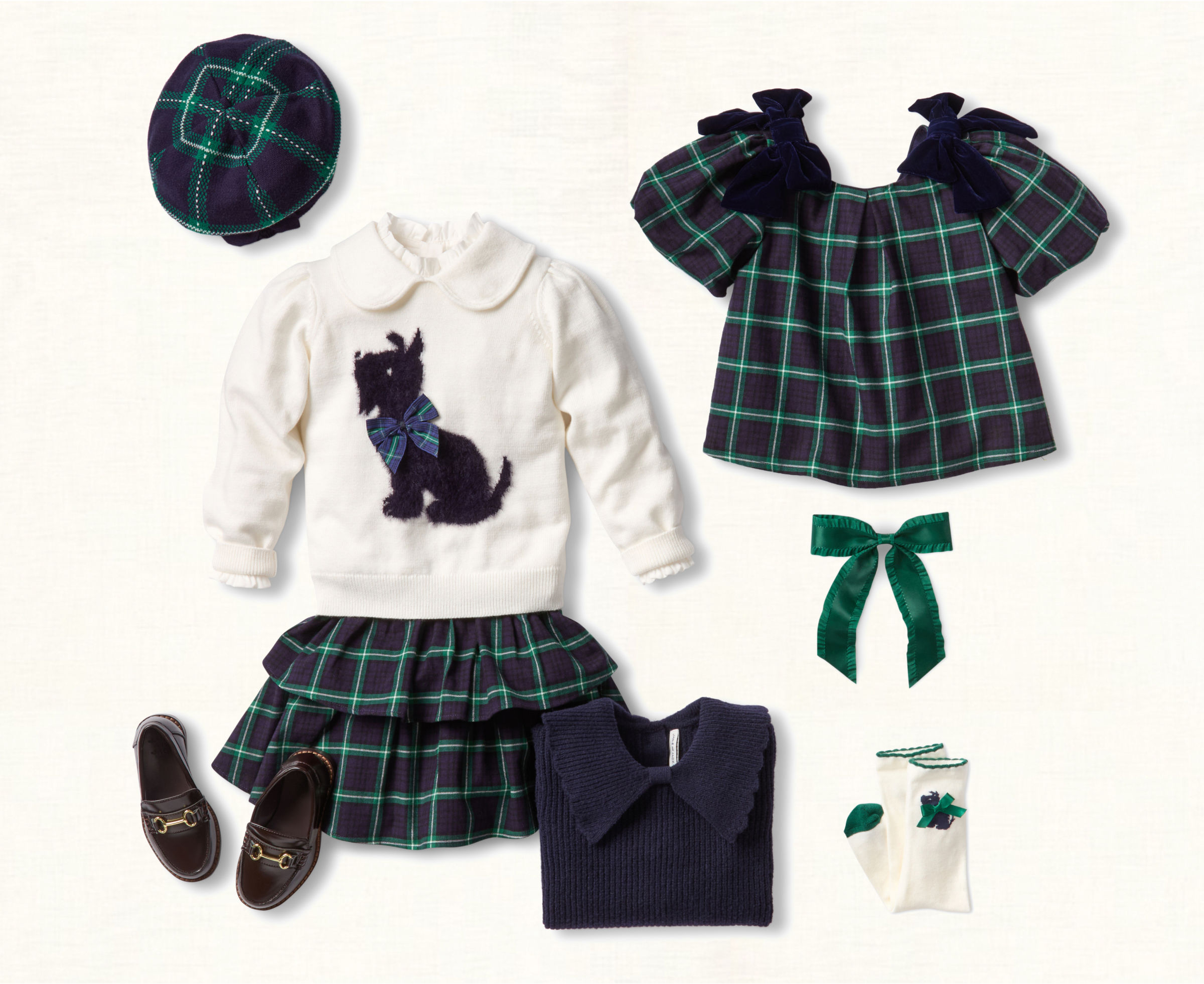 A flatlay collection of children's clothing in navy and green plaid, including a white scottie dog sweater, plaid ruffle skirt, plaid blouse with velvet bows, navy ribbed sweater, plaid beret, brown horsebit loafers, green satin hair bow, and white knee socks with scottie dog detail