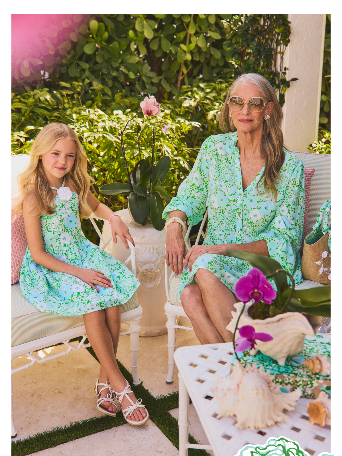 Two women in matching green floral dresses sitting on white outdoor furniture in a garden setting