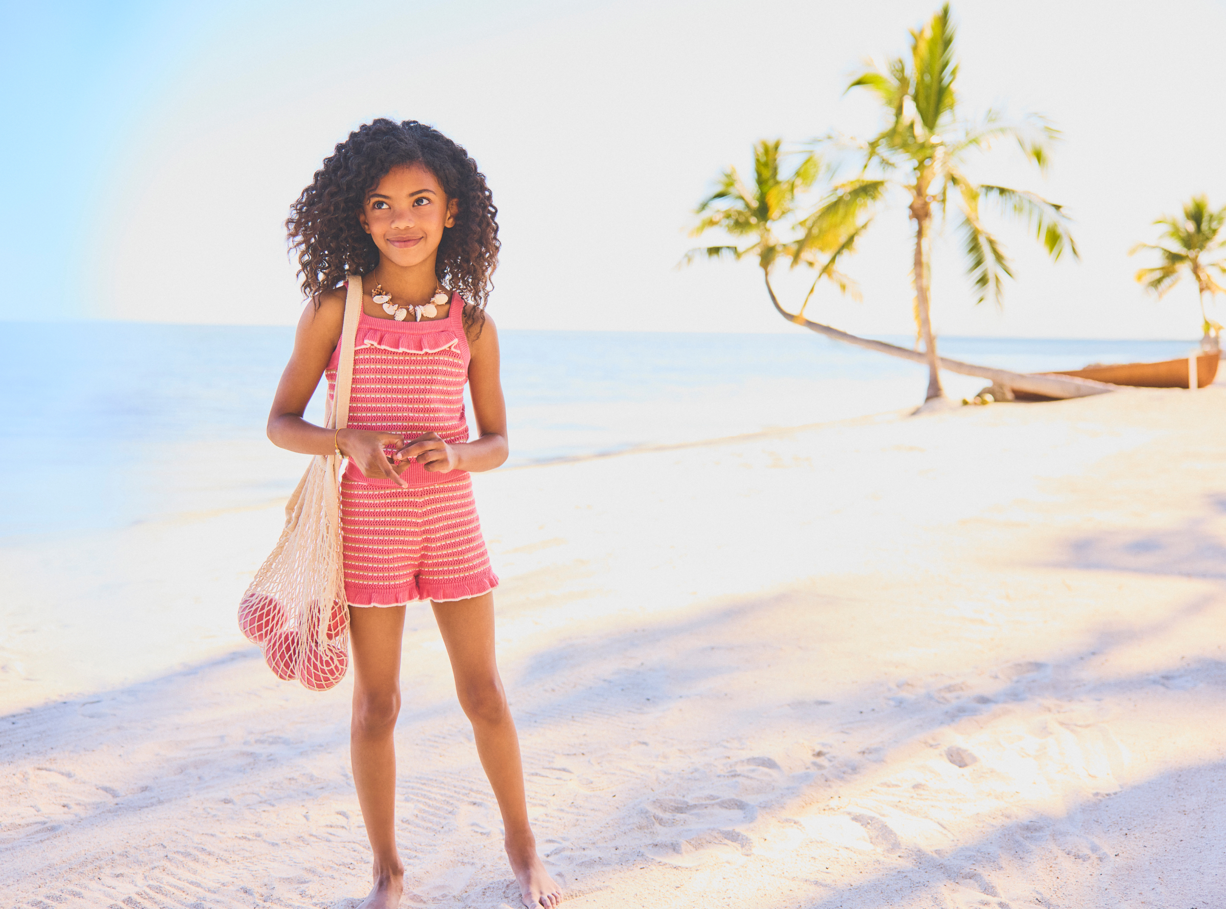 Young girl in pink striped outfit walking on tropical beach with palm trees