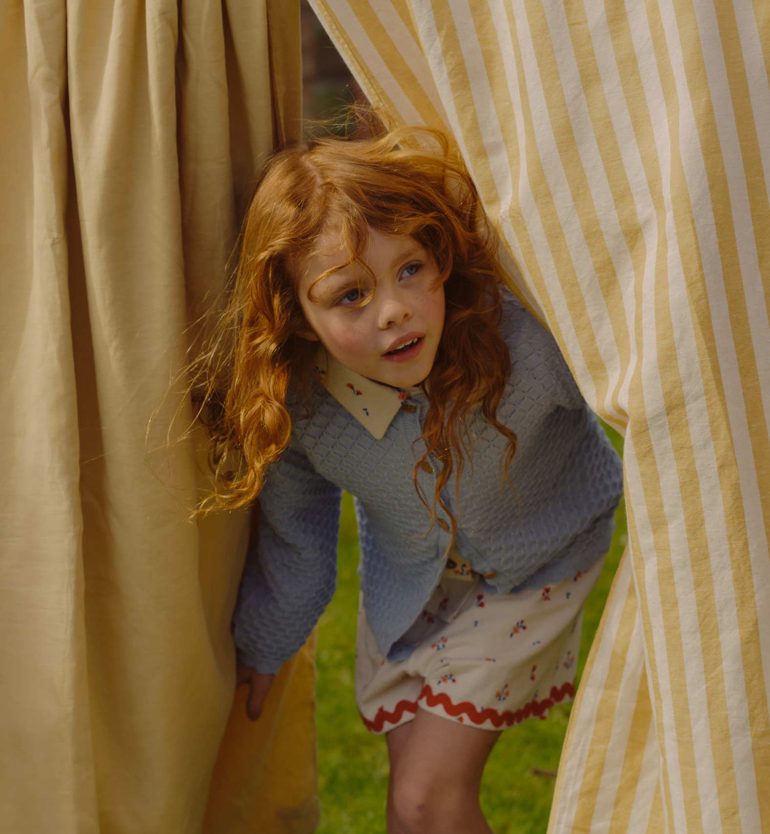 A girl peeking from between bedsheets hanging on a clothes line