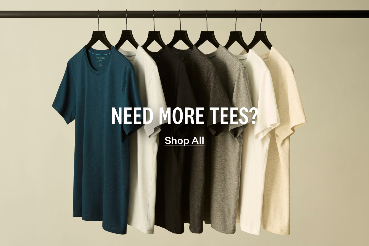 Row of Mack Weldon T-shirt collection hanging on black hangers.