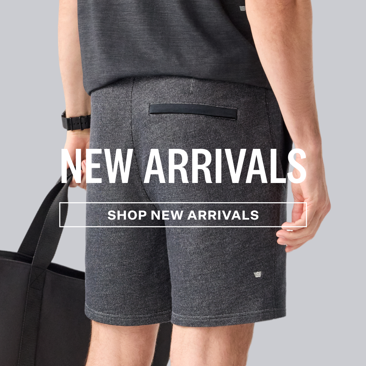 A man wearing Ace Sweatshort in True Black - Bird's Eye carrying a black bag with a large white texts "New Arrivals"  in the center