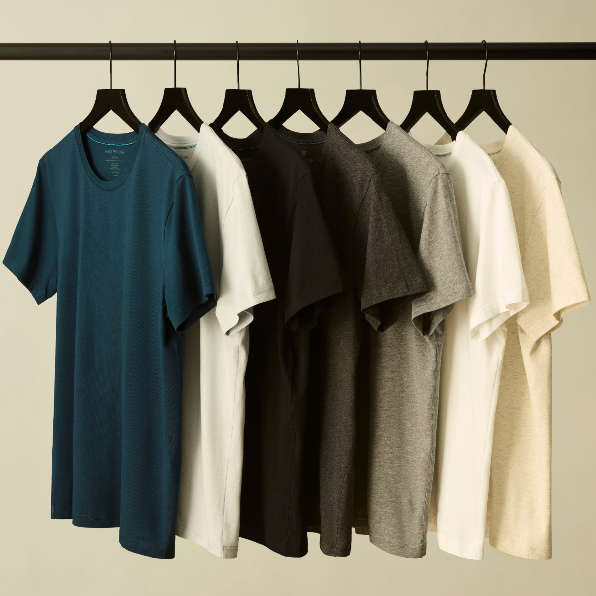 A row of Mack Weldon T-shirts hanging on black hangers 
