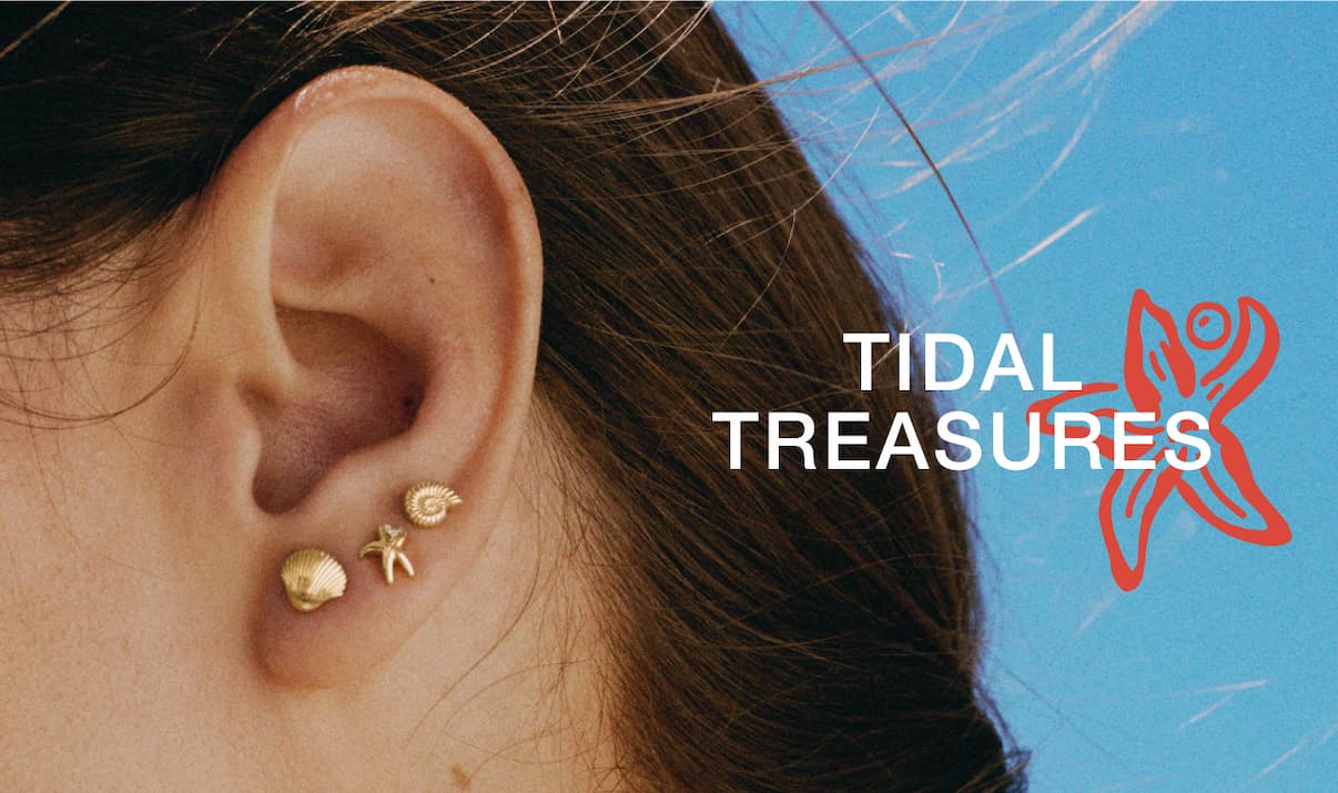 Close-up of a woman's ear styled with small Mejuri gold studs against a blue background — Tidal Treasures.