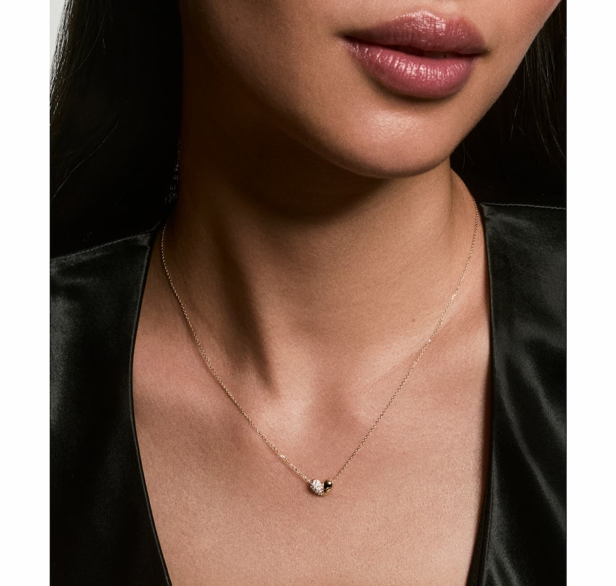 Delicate gold chain necklace with a small dark stone pendant, worn close to the collarbone.