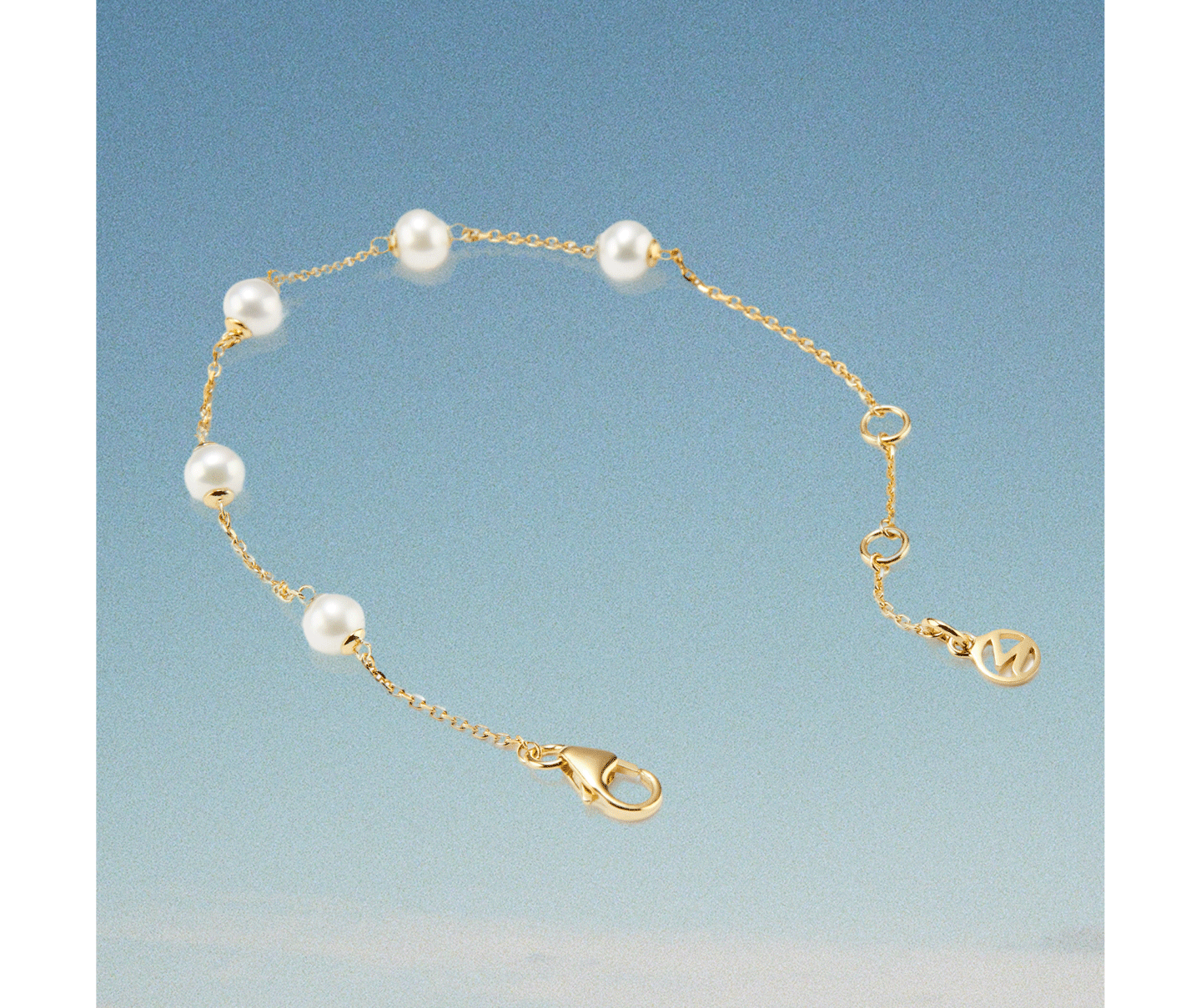 GIF cycling through Mejuri gold huggie earrings with freshwater pearl drops, a gold pearl station bracelet, and a micro pearl necklace — all against a soft blue sky background.
