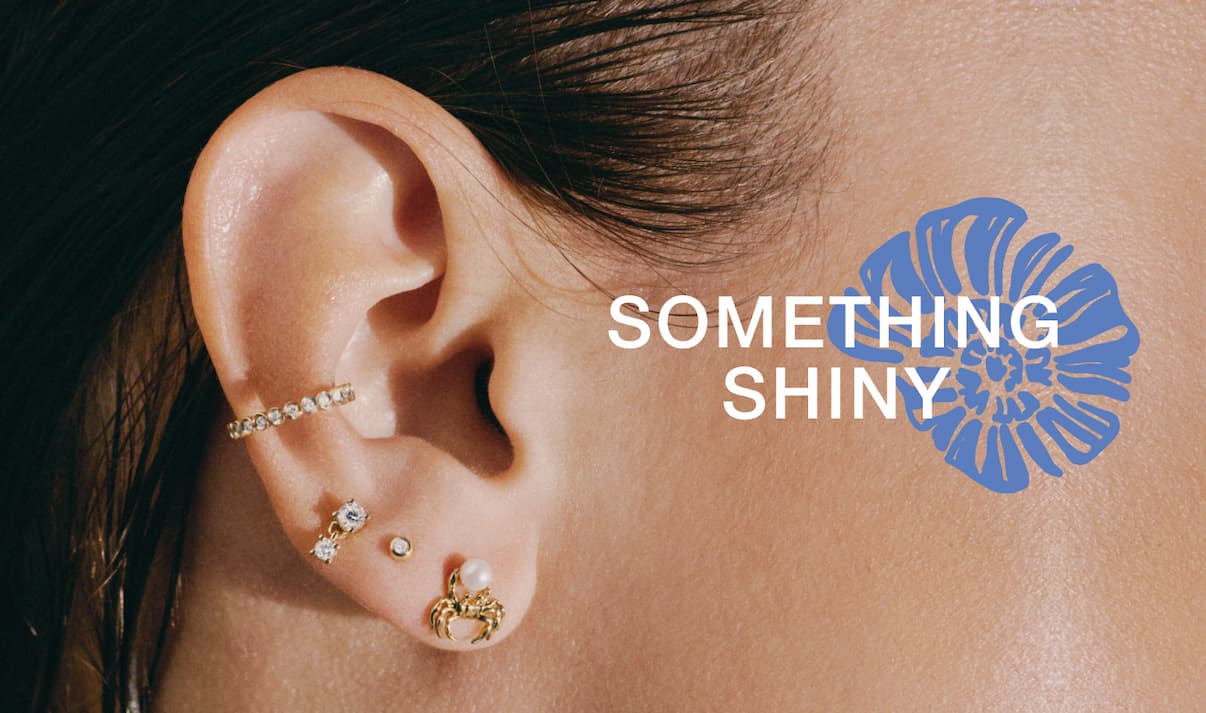 Close-up of a woman's ear styled with multiple Mejuri diamond studs and an ear cuff — Something Shiny.