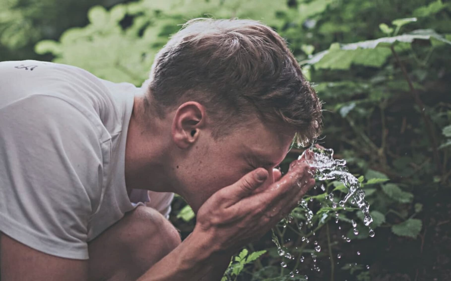 Man splashing eyes with water in a forrest