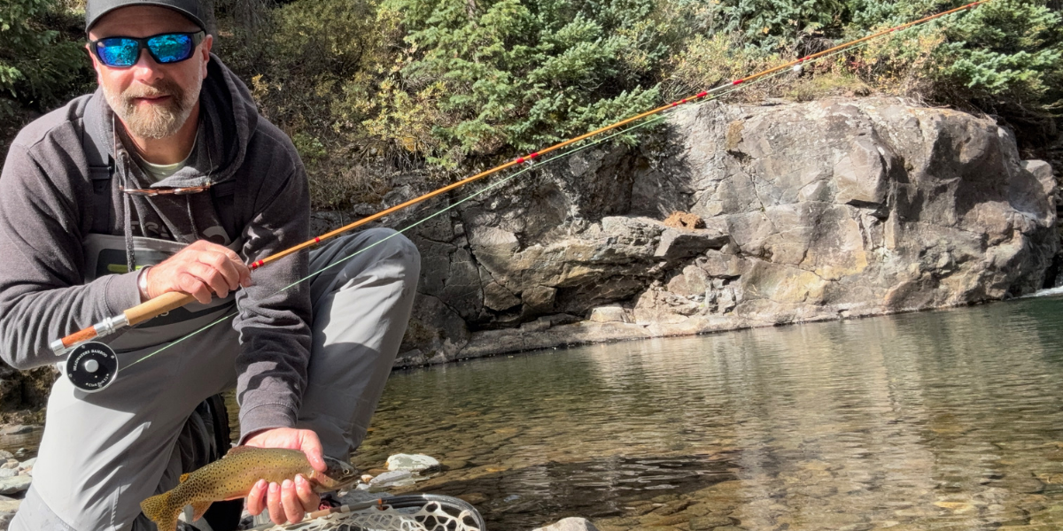 An angler with a trout on a bamboo rod