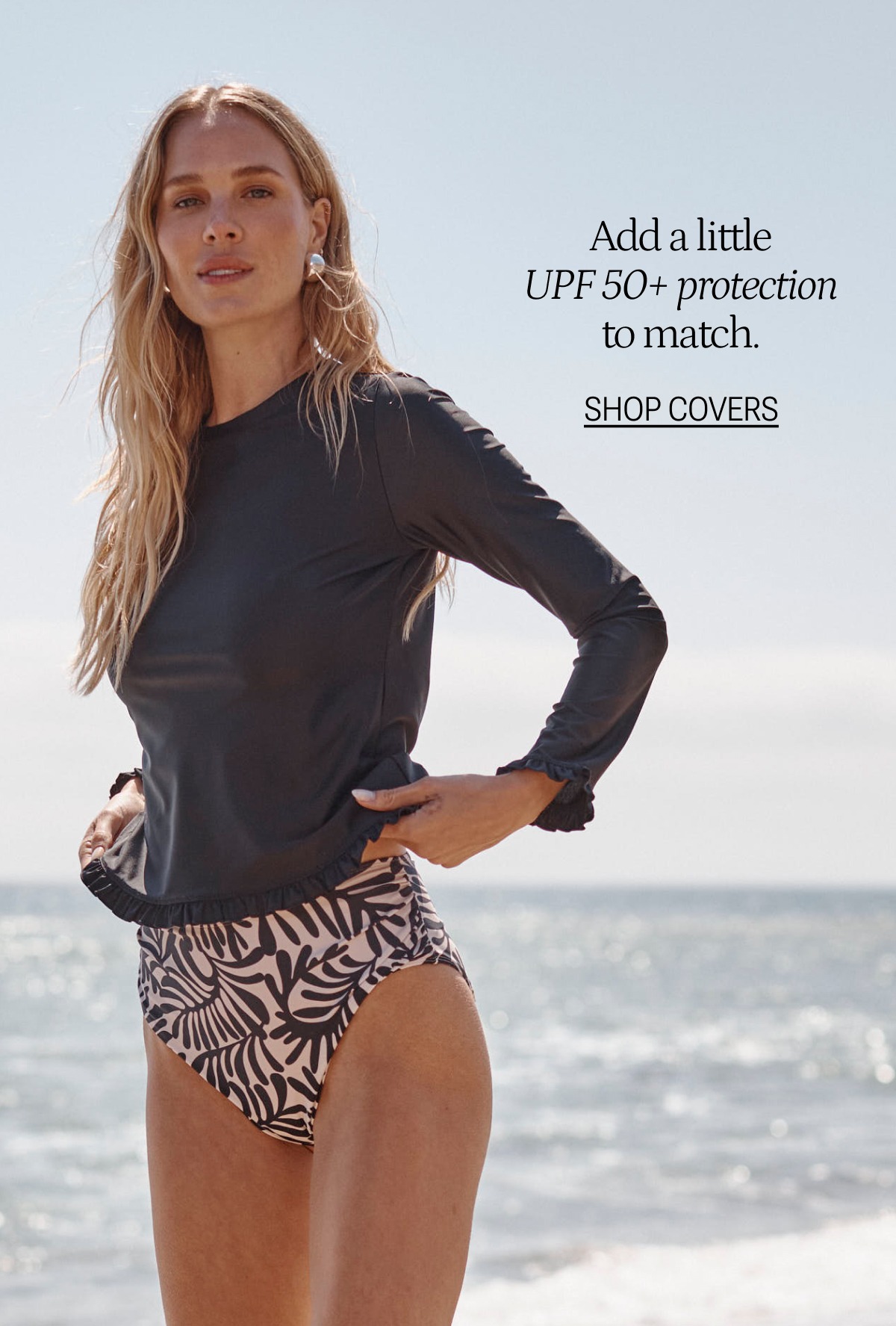 Model wearing a long sleeve rash guard and bikini bottoms on the beach