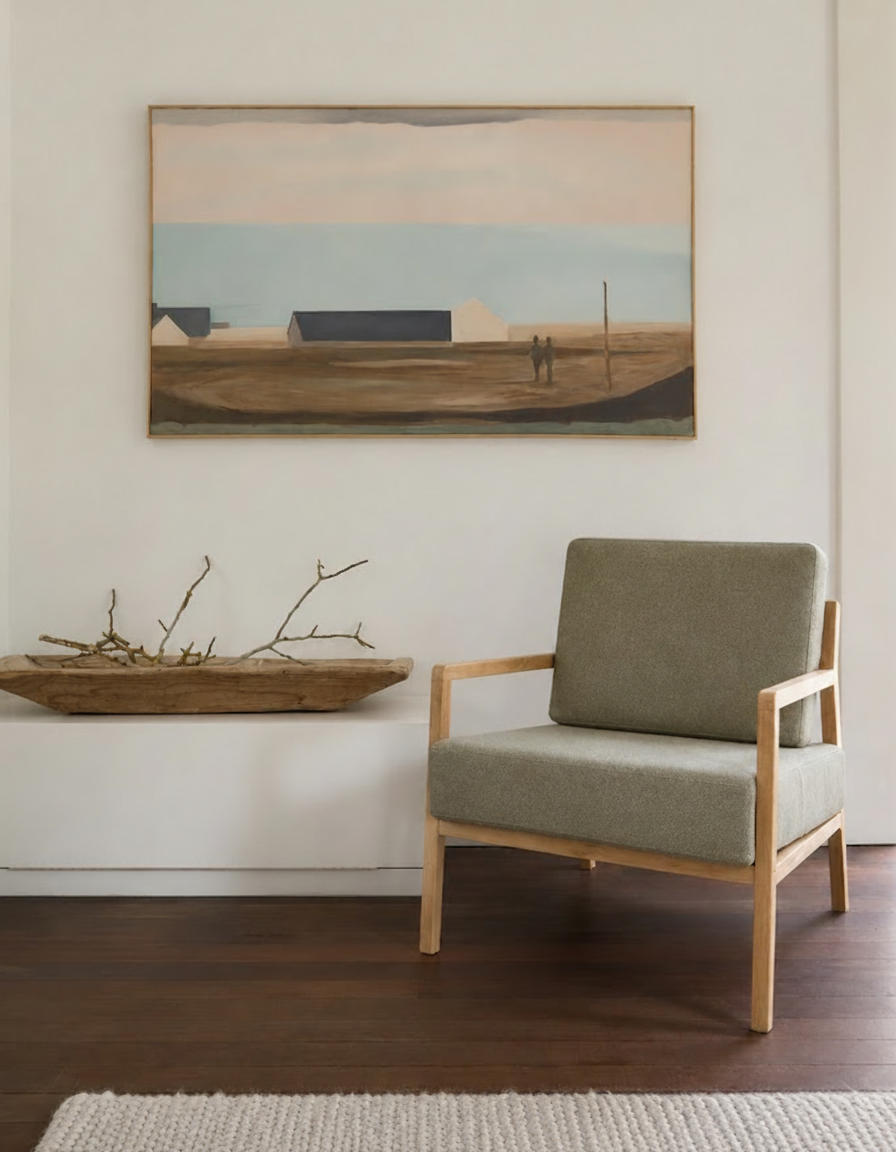 A minimalist armchair sits next to a wooden bowl with branches and a landscape painting on a white wall.