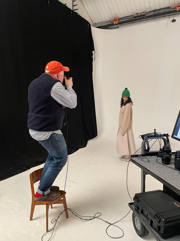Huw Morgan stands on a chair as he photographs a model wearing a green Jo Gordon hat