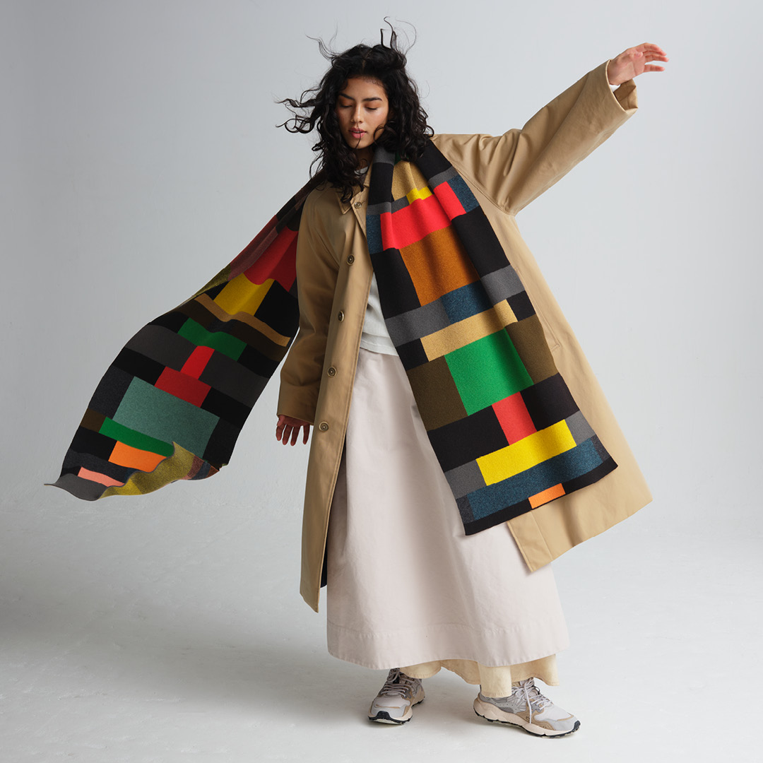 Model posing wearing a colourful AW25 Jo Gordon scarf. Their hair and the scarf are gently blown back by wind