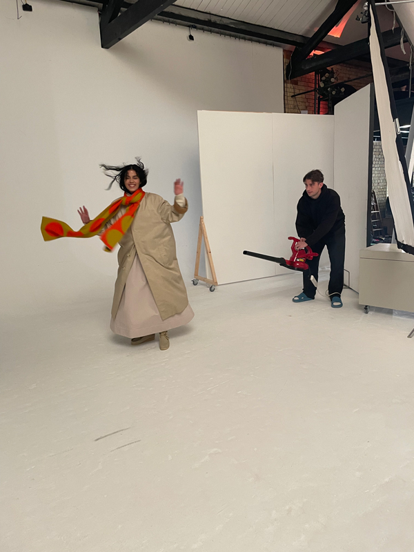 model smiles at the camera in this behind the scenes photo while someone blows air at them