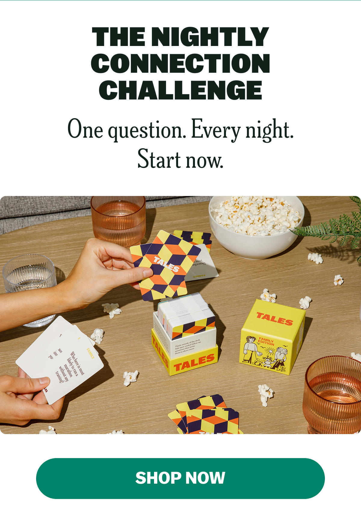 A hand holding a card game box on a table with popcorn and glasses.