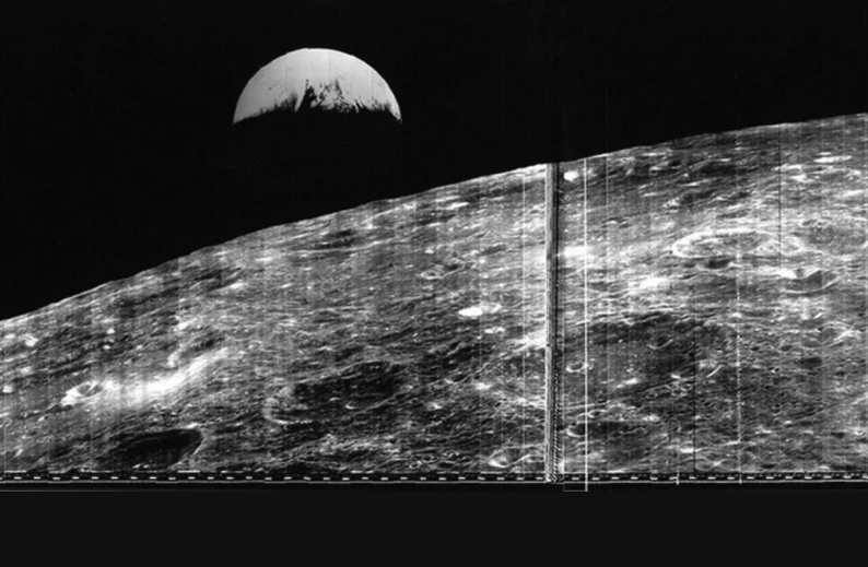 Black and white photo showing Earth rising above a grainy moon.