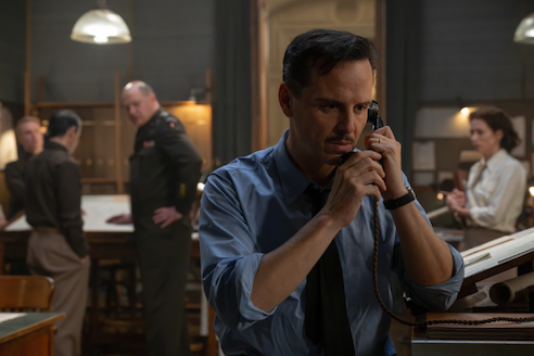 Actor Andrew Scott, in character, holds two hands to a phone at his ear. Actor Brendan Frasier, in military garb, looks on from the background.
