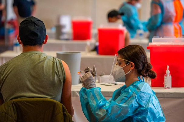 Masked healthcare worker injects vaccine into seated person's arm