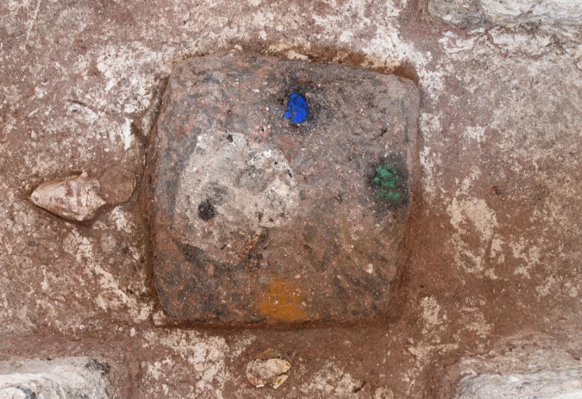 A stone square with a patch of blue to the top, green to the right, yellow at the bottom and cream-colored shell to the left