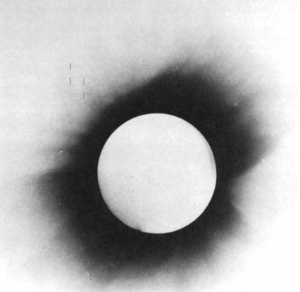 A negative image of a total solar eclipse with four faint vertical lines on the upper left edge of the sun..