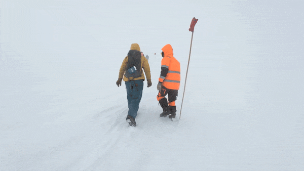 Researchers struggle across a snowy surface in near whiteout conditions.