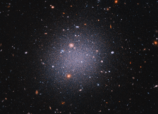 A cloud-like blur of while material against a field of galaxies in space