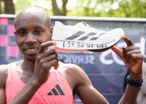 Sabastian Sawe holds up one of his white marathon running shoes. His winning time of 1:59:30 is sharpied on the side of the sole.