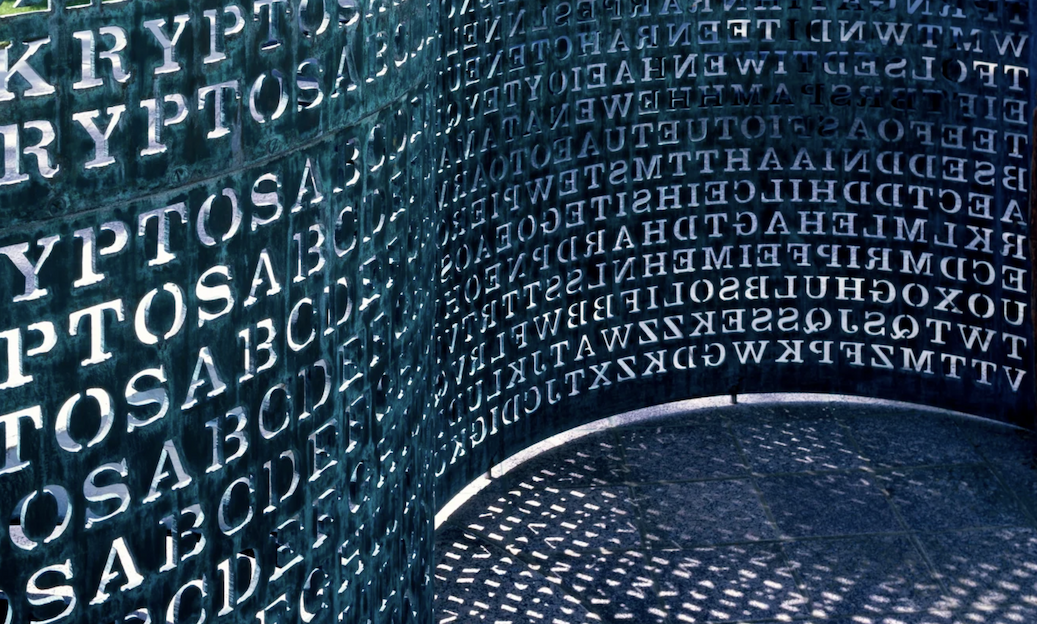 A view of the Kryptos sculpture showing a jumble of random-seeiming letters curving along a wall.